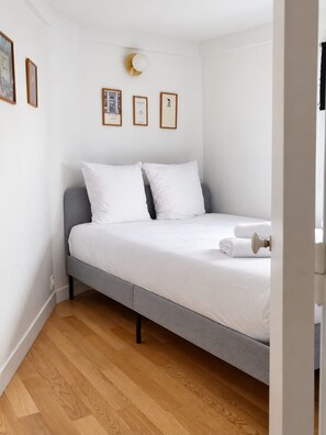 A modern bedroom with a grey bed, white bedding, and a wooden floor. - Sublim apartement Saint Germain des Prés (Paris)