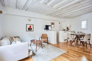 A modern living room with a white sofa, a dining table with chairs, a small rug, and a ceiling with exposed beams. - Sublim apartement Saint Germain des Prés (Paris)
