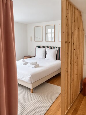 A bedroom with a bed, a wooden partition, and a white wall with two framed pictures.