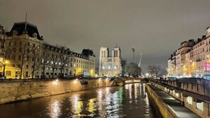 A nighttime view of a river with a bridge, buildings on either side, and a prominent cathedral in the background. - Very Charming Apartment Center of Paris Le Marais (Paris)