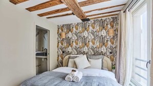 A bedroom with a bed, a wardrobe, a patterned wallpaper, and a window with curtains. - Charming apartment Center of Paris/Montorgueil (Paris)