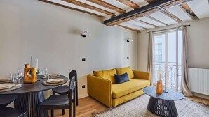 A modern living room with exposed wooden beams, a yellow sofa, a round coffee table, and a dining area with a wooden table and chairs. - Charming apartment Center of Paris/Montorgueil (Paris)