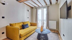 A modern living room with a yellow sofa, a round coffee table, and a large window with curtains. - Charming apartment Center of Paris/Montorgueil (Paris)