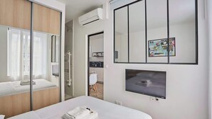 A modern hotel room with a large bed, a TV mounted on the wall, and a sliding door closet. - Charming Apartment Center of Paris-Montorgueil (Paris)