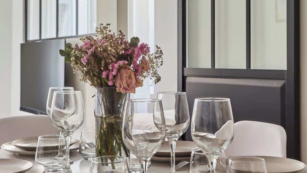A dining table set with plates, glasses, and cutlery, with a vase of flowers in the center. - Charming Apartment Center of Paris-Montorgueil (Paris)