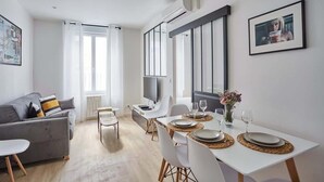 A modern living room with a grey sofa, a dining table set for four, and a TV on a stand. - Charming Apartment Center of Paris-Montorgueil (Paris)