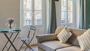 Un salón acogedor con techo de madera, un sofá, una mesa de centro de vidrio y una zona de comedor con una mesa pequeña y sillas.