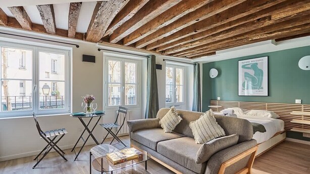 Una sala de estar acogedora con techo de madera, un sofá, una mesa de centro y un comedor con sillas y una mesa.