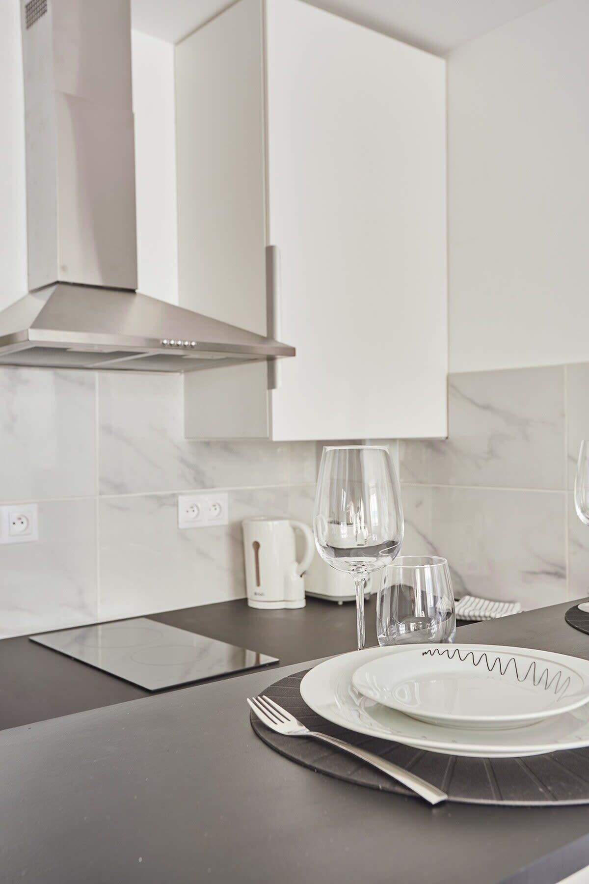 A modern kitchen with a stainless steel range hood, white cabinets, and a marble backsplash.