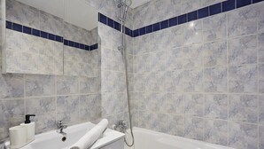 A bathroom with a bathtub, a shower, and a sink with a towel and toiletries.