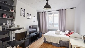 A modern hotel room with a bed, a desk with a chair, a television, and a window with curtains.