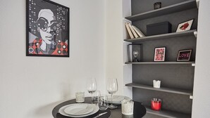 A dining area with a round table set for four, a bookshelf with various items, and a framed artwork on the wall.