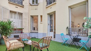 A courtyard with artificial grass, wicker chairs, a small table, and potted plants. - Eiffel Tower Terrace Apartment (Paris)