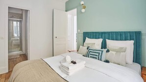 Een slaapkamer met een bed, een blauwgroen hoofdeinde en een witte deur.