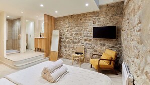 A modern bedroom with a stone wall, a flat-screen TV, a bed with rolled towels, a wooden chair, and a small table with a mirror. - Amazing apartment in the Center of Paris ( Marais) (Paris)