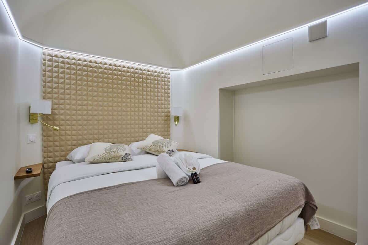 A neatly made bed with a beige headboard, white bedding, and a pair of towels on the bed.