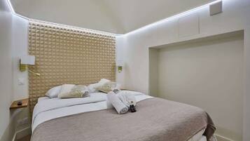 A neatly made bed with a beige headboard, white bedding, and a pair of towels on the bed.