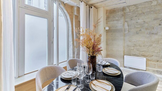 A dining area with a round table set for four, a vase with dried flowers, and a stone wall in the background. - Amazing apartment in the Center of Paris ( Marais) (Paris)