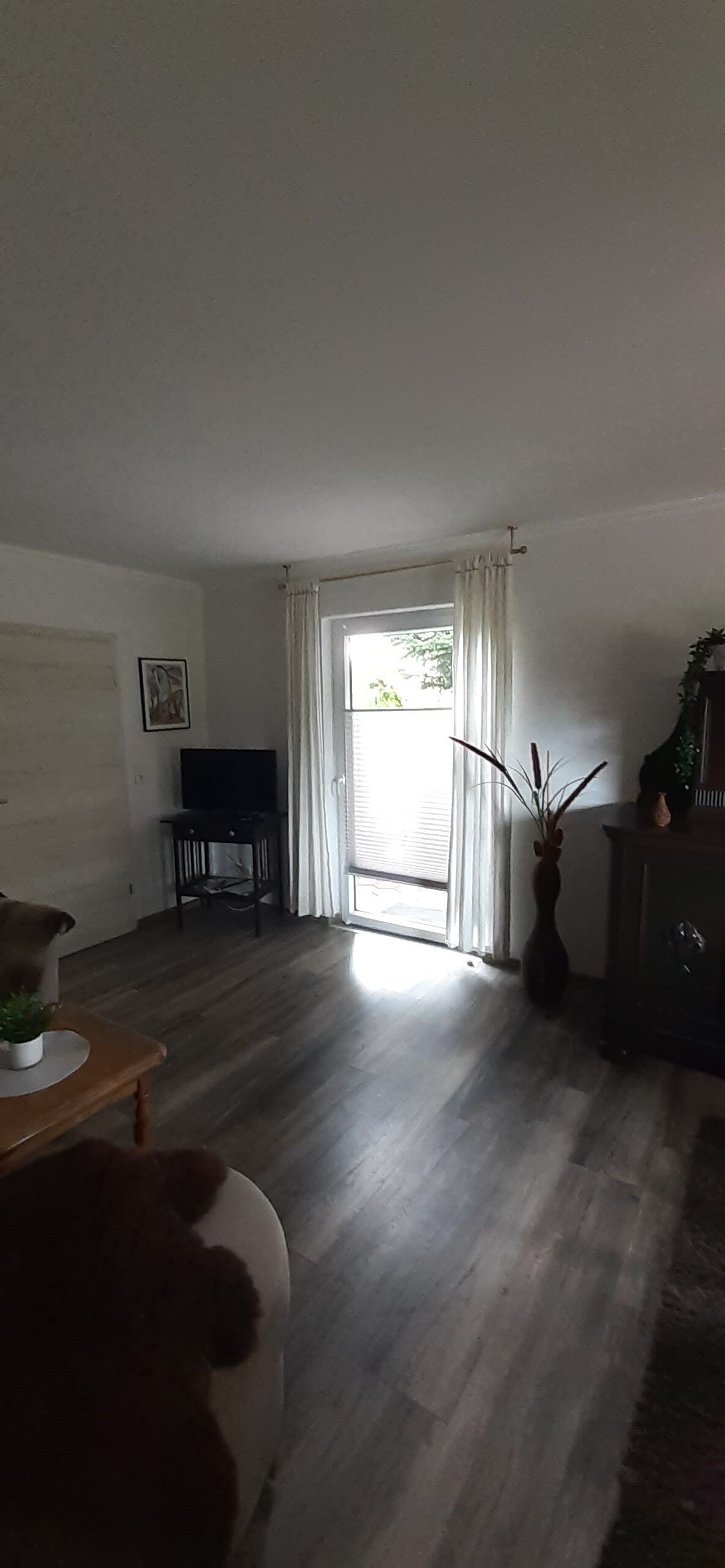 A living room with a wooden floor, a television, a sofa, a cabinet, and a window with curtains.