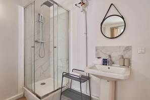 A bathroom with a glass-enclosed shower, a sink with toiletries, and a wall-mounted mirror.