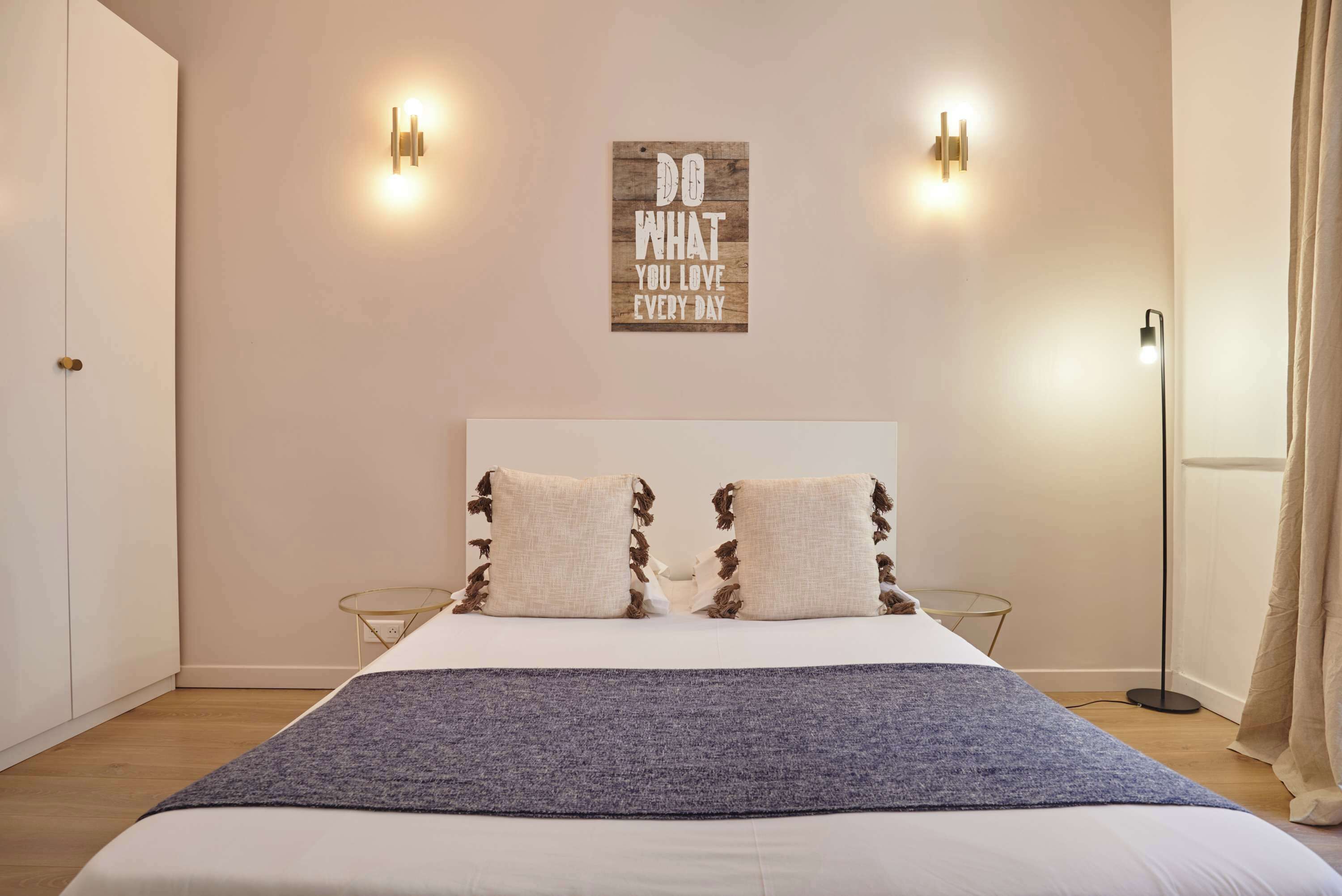 Een slaapkamer met een bed, twee wandlampen, een inspirerende quote en een vloerlamp.