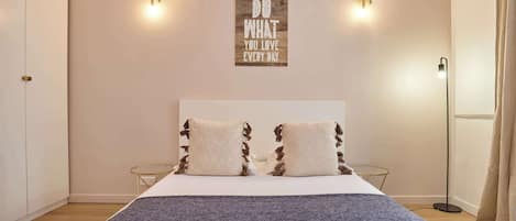 Une chambre à coucher avec un lit, deux lampes fixées au mur, une citation inspirante et une lampe sur pied.