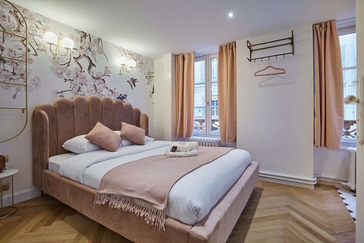 Une chambre à coucher avec un grand lit, un radiateur, une fenêtre avec des rideaux et un luminaire fixé au mur.
