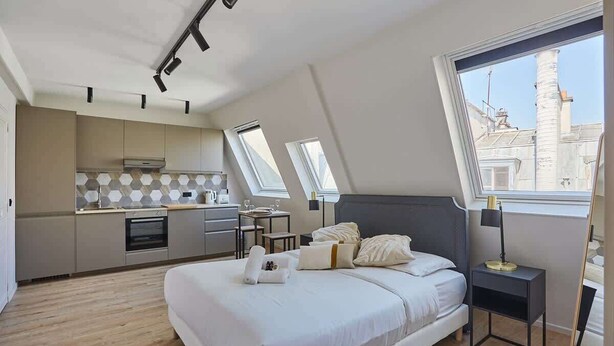 Un dormitorio moderno con una cama grande, una mesita de noche y vistas a la ciudad desde una ventana.