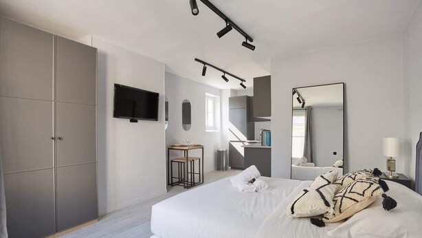 Ein modernes Hotelzimmer mit einem großen Bett, einem Fernseher, einem Schreibtisch und einem durch eine offene Tür einsehbaren Badezimmer.
