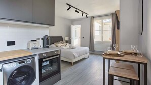Ein kleines Hotelzimmer mit Küchenzeile, einem Bett, einer Essecke und einem großen Fenster.