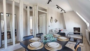 A dining area with a black table set for four, surrounded by chairs, and a small side table with a plant. - Sublim apartment Beaubourg/Le Marais (Paris)