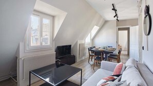 A modern loft apartment with a sloped ceiling, a dining area, a sofa, and a TV. - Sublim apartment Beaubourg/Le Marais (Paris)