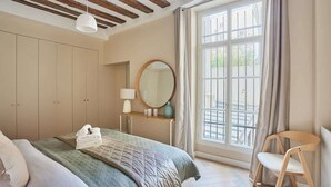Ein Schlafzimmer mit Bett, Nachttisch, Spiegel und einem Fenster mit Vorhängen.