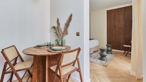 Ein Essbereich mit einem runden Holztisch, zwei Korbstühlen und einer Vase mit Trockenpflanzen.