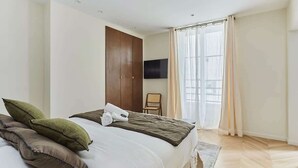 Ein Hotelzimmer mit Bett, Wandfernseher, Holzschrank und einem Fenster mit Vorhängen.