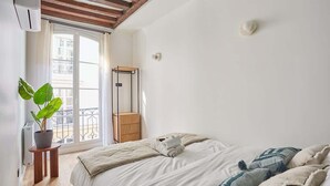 A bedroom with a bed, a potted plant, a wooden nightstand, and a window with a view of a balcony. - New Apartment Center of Paris Place de la Bourse (Paris)