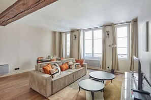 Uma sala de estar ampla com um sofá grande, duas mesas redondas e uma lareira.