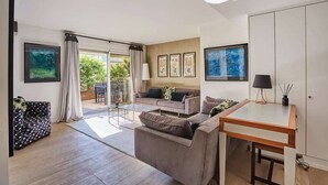 A modern living room with a sofa, a coffee table, and a dining area with a table and chairs. There is a sliding glass door leading to an outdoor area with a garden. - Amazing Penthousse Foch/Arc de Triomphe/ Trocadero (Paris)