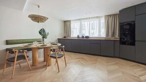 A modern kitchen with a dining area, featuring a herringbone wood floor, a green cushioned bench, and a pendant light. - Spacious AC flat Luxembourg St Germain des près (Paris)