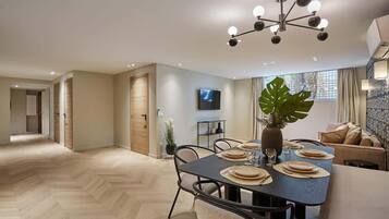 Un espace repas moderne avec une grande table dressée pour quatre personnes, un lustre et une plante en pot.