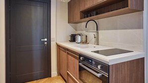 A compact kitchen with a dark door, wooden cabinets, a white countertop, a built-in oven, and a sink.