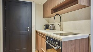 A compact kitchen with a dark door, wooden cabinets, a stainless steel sink, a kettle, and a built-in oven. - New apartment Center of Paris/Le Marais (Paris)