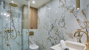 A modern bathroom with a glass-enclosed shower, a marble wall, a wooden cabinet, and a gold faucet. - New apartment Center of Paris (Paris)
