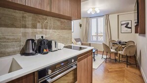 A modern kitchen with a built-in oven, a coffee maker, and a kettle. There is a dining area with a table and chairs. - New apartment Center of Paris (Paris)