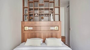 Un dormitorio con cabecera de madera, dos almohadas blancas y una estantería empotrada sobre la cama.