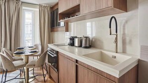 Una cocina compacta con armarios de madera, encimera blanca, pileta y un comedor con una mesa redonda y sillas.