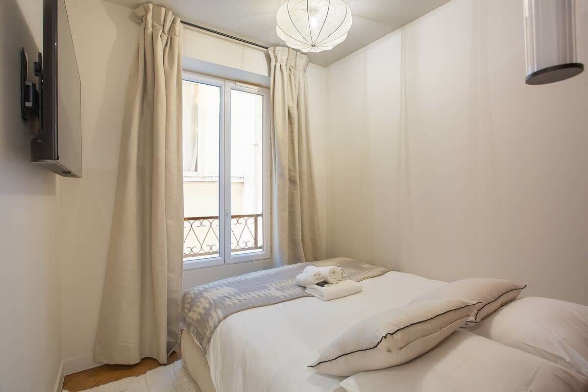 A bedroom with a bed, curtains, a window, and a ceiling light.