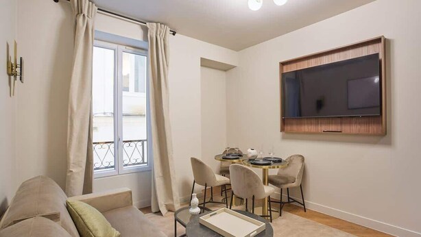 A modern living room with a sofa, a small round table, and a TV mounted on the wall.