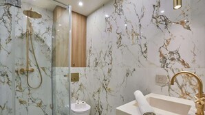 A modern bathroom with a glass-enclosed shower, marble walls, and a gold faucet.