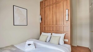 Une chambre d’hôtel avec une tête de lit en bois, un lit recouvert de draps blancs et une œuvre d’art encadrée accrochée au mur.